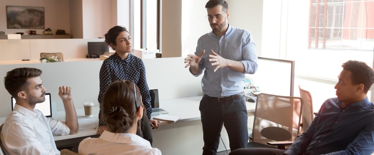 Serious business man team leader coach mentor talk to diverse business people in office explain strategy at corporate group meeting, multiethnic staff listen to boss instruct interns at briefing